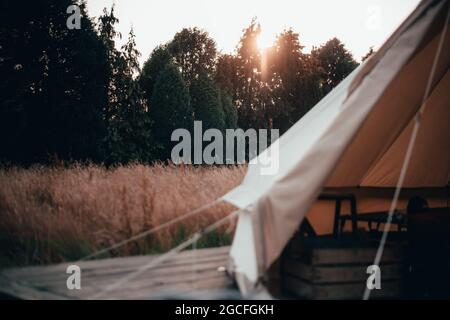 All'interno di una tenda campanaria usata per glamping e campeggio in un lungo campo d'erba con il tramonto dietro la tenda Foto Stock