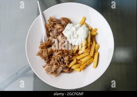 Donare le fette di carne kebab dallo spiedo torrefante a rotazione con patatine fritte e il dip di yogurt tzatziki, servito su un piatto bianco in un ristorante turco fast food Foto Stock