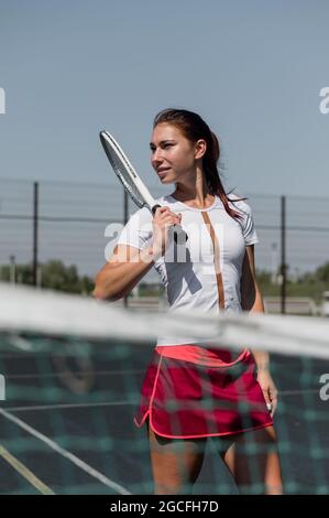 Bella donna sorridente con un'ombra da una racchetta da tennis sul viso in una giornata di sole Foto Stock