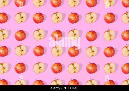 Eccezionale motivo di mele intere fresche e di metà di mele su sfondo rosa. Concetto di cibo sano minimalista. Disposizione piatta Foto Stock