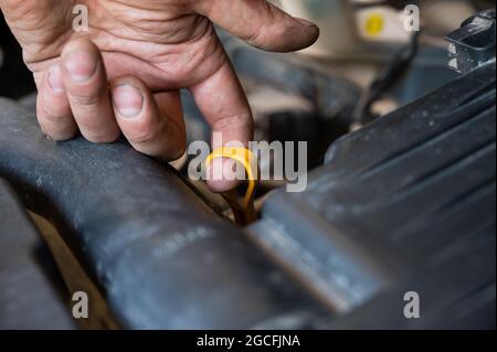Un meccanico automatico tira fuori un'astina di livello per controllare il livello dell'olio in un motore di automobile. Foto Stock