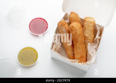 Pubblicità fritto, malsano fast food, da asporto e consegna dei pasti. Bastoncini di formaggio appetitosi in scatola di cartone eco con diverse salse in contenitori Foto Stock