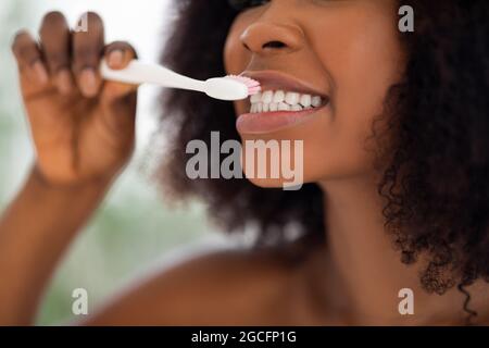 Concetto di igiene dentale. Vista ritagliata della giovane donna nera che pennellava i denti all'interno, primo piano. Irriconoscibile donna afro che si prende cura della sua salute, per Foto Stock