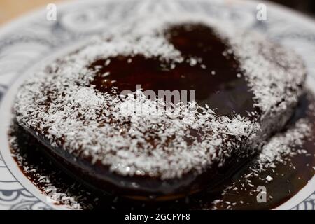 Torta fatta in casa con motivo di glassa al cioccolato a forma di cuore e patatine di cocco. Deliziosi dolci. Foto Stock