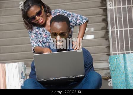 Una coppia felice che usa un computer portatile seduto all'esterno e che passa il tempo insieme dopo aver fatto uno shopping Foto Stock