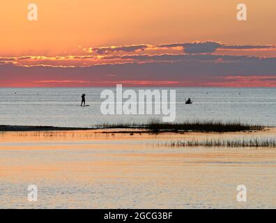 Silhouette di un uomo su una tavola da surf e di un uomo in un kayak che pesca a Cape Cod Bay mentre il sole tramonta da Paine's Creek Beach, Brewster, Massachusetts Foto Stock