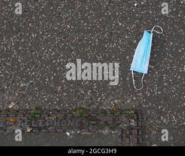 Facemask visto scartato sulla strada. Foto Stock