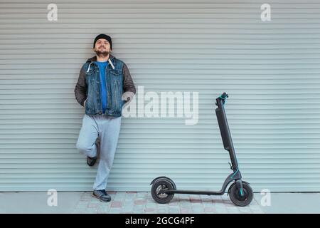 lo scooter elettrico si trova vicino al garage e un uomo è accanto ad esso. ecologia e concetto di movimento Foto Stock