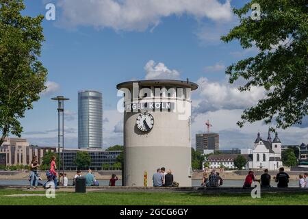 Vista soleggiata all'aperto di Pegelturm, della Torre di Pegel e della gente si siedono intorno al Giardino del Reno lungo il fiume Reno a Colonia, in Germania. Foto Stock