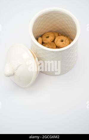 Una vista dall'alto di un piccolo contenitore bianco in ceramica con coperchio riempito di biscotti isolati su bianco Foto Stock