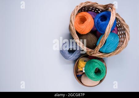 Un mucchio di palle tessili colorate di lana in un cesto di vimini su sfondo grigio con uno spazio di copia Foto Stock