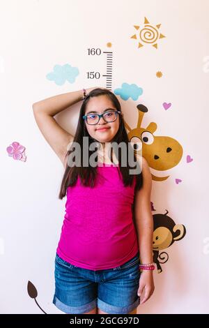 Ragazza ispanica teenager con sindrome di Down che misura la sua altezza sul muro, in concetto di disabilità in America Latina Foto Stock