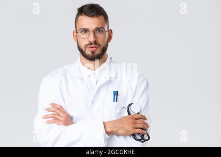 Operatori sanitari, coronavirus, covid-19 pandemia e concetto di assicurazione. Primo piano di serio medico giovane in camice bianco, bicchieri, ascoltare da vicino Foto Stock