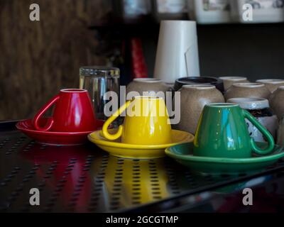 Tazza di caffè in ceramica gialla, verde e rossa capovolta sul piattino sulla mensola in metallo del caffè. Foto Stock