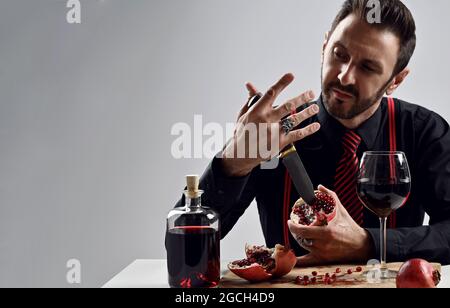 Uomo brutale non rasato, mafioso in camicia nera con cravatta a righe e sospetti al tavolo bastoni coltello a melograno fresco Foto Stock