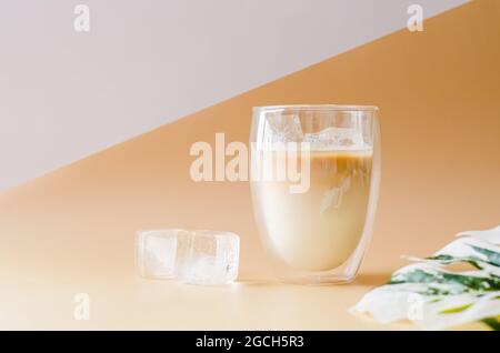Cubo ghiacciato in un bicchiere che copre con vapore di caffè latte con foglia di monstera e cubo ghiacciato sul pavimento. Concetto di bevanda estiva. Foto Stock