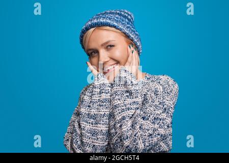 Donna bionda con cappello a maglia e stile hipster su sfondo blu. Bella giovane donna. Outfit donna. Foto Stock