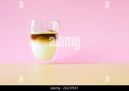 Un bicchiere che copre con un po' di vapore di caffè mescolando il latte su sfondo marrone e rosa. Concetto di bevanda estiva. Foto Stock