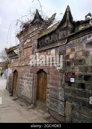 Un antico edificio nel quartiere di Lizhuang con vecchie mura, porte in legno e mattoni coltivati con piante e felci. Foto Stock