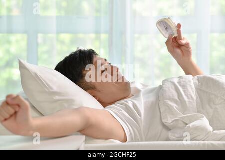 Ritratto dell'uomo asiatico felice che si sveglia a letto al mattino Foto Stock