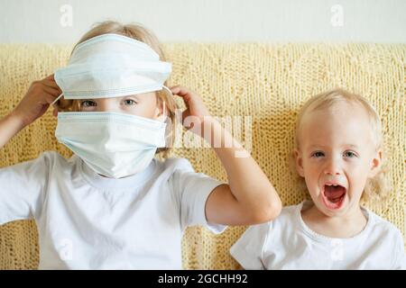 Ritratto di due sorelle che indossano maschere protettive mediche. La sorella maggiore aiuta i più giovani. Sorelle che giocano divertimento. Concetto di protezione del coronavirus Foto Stock