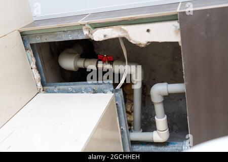 tubo flessibile in plastica nel portello nel soffitto. sostituzione del montante e dei tubi attraverso le piastrelle tagliate nel soffitto. Valvola a sfera rossa su un Pex-al Foto Stock