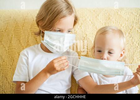 Ritratto di due sorelle che indossano maschere protettive mediche. La sorella maggiore aiuta i più giovani. Sorelle che giocano divertimento. Concetto di protezione del coronavirus Foto Stock