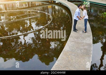 Felice giovane coppia multietnica innamorata di tenere le mani e baciarsi quando si cammina nel parco della città Foto Stock