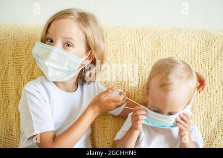 Ritratto di due sorelle che indossano maschere protettive mediche. La sorella maggiore aiuta i più giovani. Sorelle che giocano divertimento. Concetto di protezione del coronavirus Foto Stock