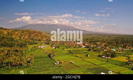 Maestoso vulcano Gunung Agung a Bali che torreggia in alto sopra i dintorni. Campi di riso allagati con acqua. Lussureggiante vegetazione tropicale e giungla Foto Stock