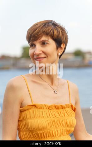 Ritratto di allegra signora di mezza età in piedi vicino al fiume in città argine, godendo l'estate Foto Stock