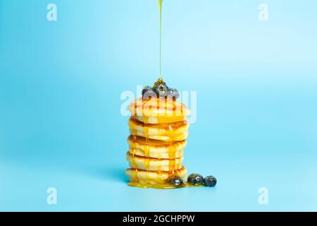 Frittelle con frutti di bosco su sfondo blu. Deliziosi pancake con mirtilli e sciroppo per il brunch su uno sfondo di colore minimo. Bella foto di cibo luminoso. Foto di alta qualità Foto Stock