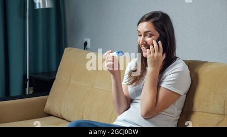 Donna felice che parla al telefono tenendo il test di gravidanza in mani Foto Stock