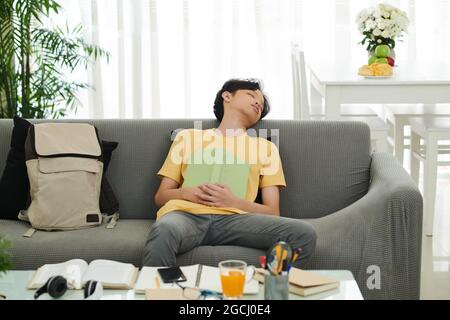 Il ragazzo adolescente si addormentò dopo aver letto il libro e essersi preparato per l'esame a casa Foto Stock