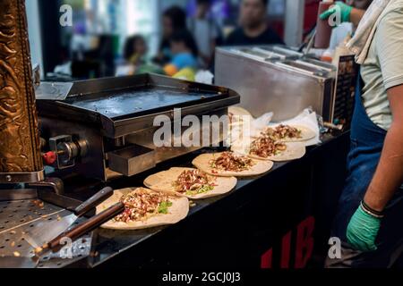 Preparazione dello shawarma turco. Tortillas pronte con cetrioli e ripieni attendono il cuoco per aggiungere la carne fritta tritata e versare il piattino Foto Stock