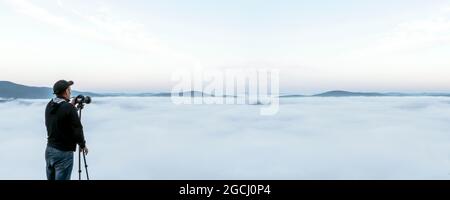 un uomo rimuove la nebbia sulla macchina fotografica. un viaggiatore fotografa un bellissimo paesaggio desertico nebbioso in montagna la mattina presto. foschia di nuvole a. Foto Stock