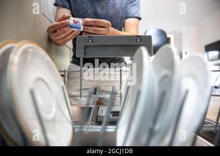 Un uomo davanti a una lavastoviglie aperta può contenere una compressa di detersivo per piatti in lavastoviglie. Foto Stock