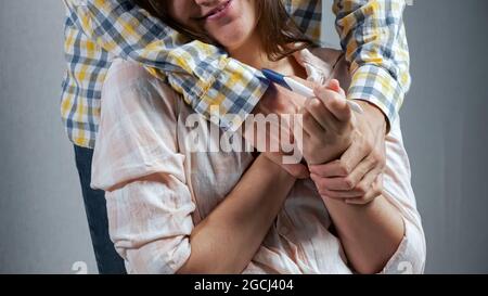 la donna si siede con un test di gravidanza. l'uomo dietro è felice del risultato Foto Stock