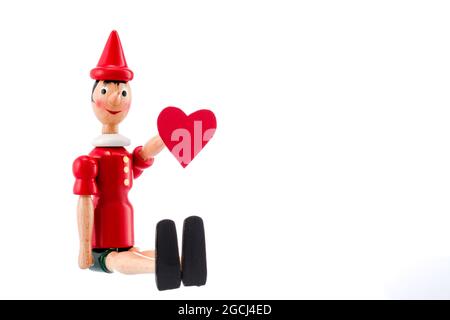 Pinocchio toy statua e cuore isolato su sfondo bianco. Il giorno di San Valentino del concetto. Foto Stock