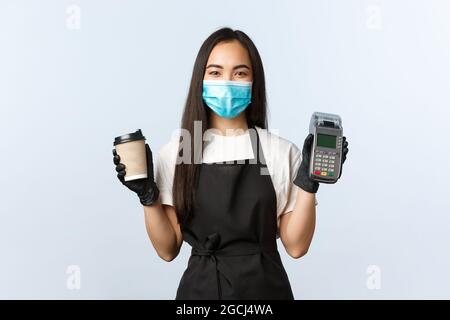 Caffetteria, coronavirus, approccio sociale e concetto di pagamento senza contatto. Barista sorridente e cordiale in maschera medica e guanti che tengono il tuo take-away Foto Stock