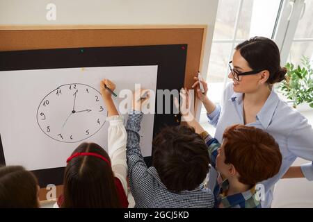 Gruppo di studenti delle scuole elementari che disegnano un orologio e imparano a raccontare l'ora Foto Stock