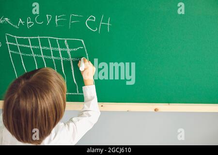 Lezione di Scacchi per bambini. Boy disegna una scacchiera sulla tavola verde in classe. Foto Stock