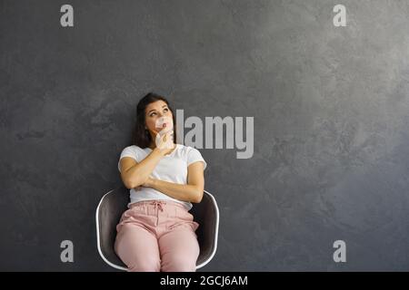 Giovane donna che guarda in su alla parete dello spazio della copia, che pensa, dubitando, che mette in discussione qualcosa Foto Stock