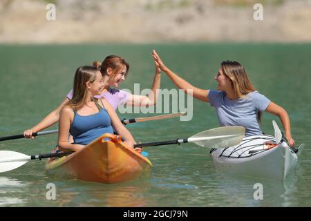 Tre amici che danno cinque godendo una giornata di kayak in un bellissimo lago in vacanza estiva Foto Stock