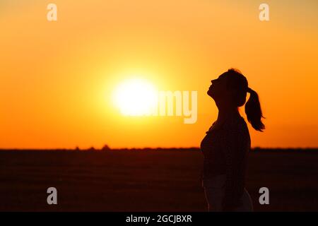 Vista laterale indietro luce ritratto di una silhouette donna che respira aria fresca all'alba Foto Stock