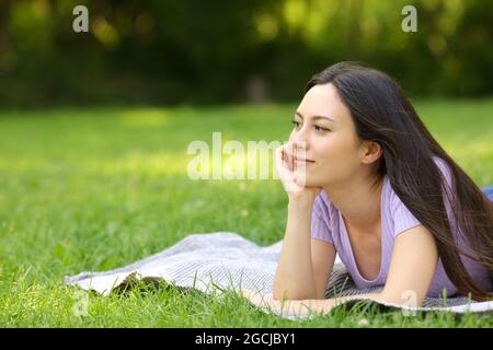 Razza mista donna contemplando e pensando sdraiato sull'erba in un parco Foto Stock