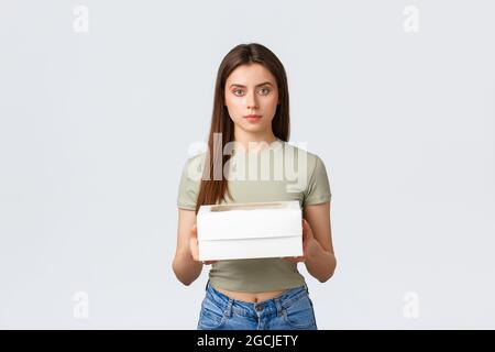 Consegna, stile di vita e concetto di cibo. Elegante giovane bella donna che tiene scatola con cupcakes, dessert ordine dal caffè preferito. Ragazza ricevere a casa Foto Stock