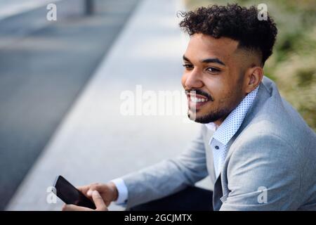 Ritratto di un giovane seduto all'aperto in città, utilizzando uno smartphone. Foto Stock