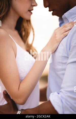 Vista laterale del raccolto giovane multietnico sposa e sposo abbracciare teneramente mentre hanno momenti romantici insieme Foto Stock