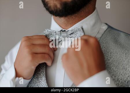 Ritagliare un uomo con la bearded irriconoscibile in elegante gilet e camicia bianca che regola la cravatta di prua mentre si prepara per la celebrazione del matrimonio Foto Stock